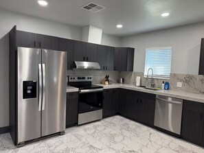 A modern kitchen with dark cabinetry, stainless appliances, and a marble backsplash.
