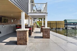 Eine überdachte Terrasse im Freien mit Grillplatz, Blick auf den Pool und Holzzaun.
