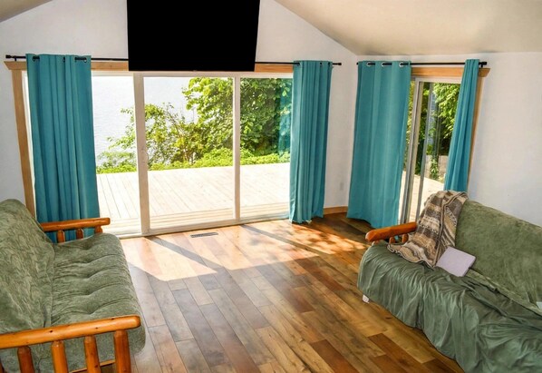 A room with two green sofas, a wooden floor, and a large sliding glass door leading to an outdoor deck.