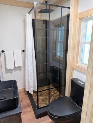 Un bagno con cabina doccia in vetro, un water nero e un lavandino nero.
