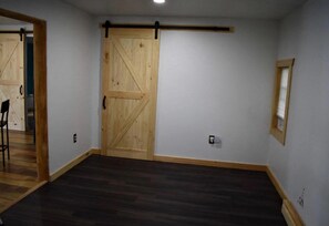 A room with a wooden door, a window with blinds, and a dark wooden floor.