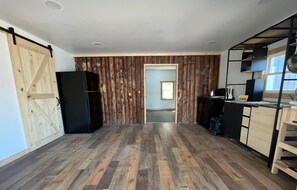 A kitchen with wooden flooring, a black refrigerator, and a wooden door.
