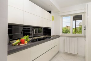 A modern kitchen with white cabinets, a black countertop, and a window with a view of greenery. - Villa Bella Cerovlje (Istria - Cerovlje) (Cerovlje)