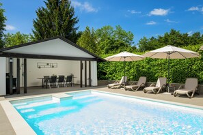 A pool area with lounge chairs and umbrellas, a covered seating area with tables and chairs, and a backdrop of greenery. - Villa Bella Cerovlje (Istria - Cerovlje) (Cerovlje)