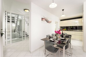 A modern dining area with a glass table, chairs, and a chandelier.