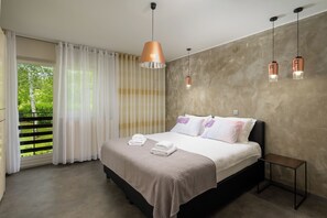 Une chambre moderne avec un grand lit, une vue sur la verdure par la fenêtre et un balcon.