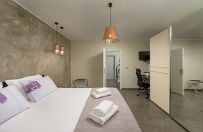 A modern hotel room with a large bed, a desk, a chair, a TV, and a bathroom visible through an open door.