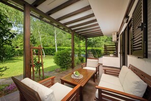 Un espacio de estar al aire libre cubierto, con muebles de madera y vista a un jardín exuberante.