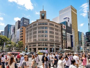 A busy urban street with a historic building featuring a clock tower, surrounded by modern high-rise buildings. - VAYS GINZA TSUKIJI TOKYO (Tokyo)