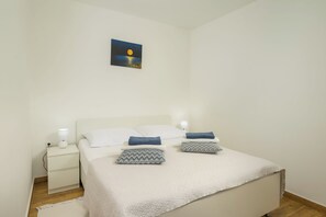 Un dormitorio con una cama, dos mesitas de noche, una lámpara de noche, un cuadro en la pared y una alfombra blanca.
