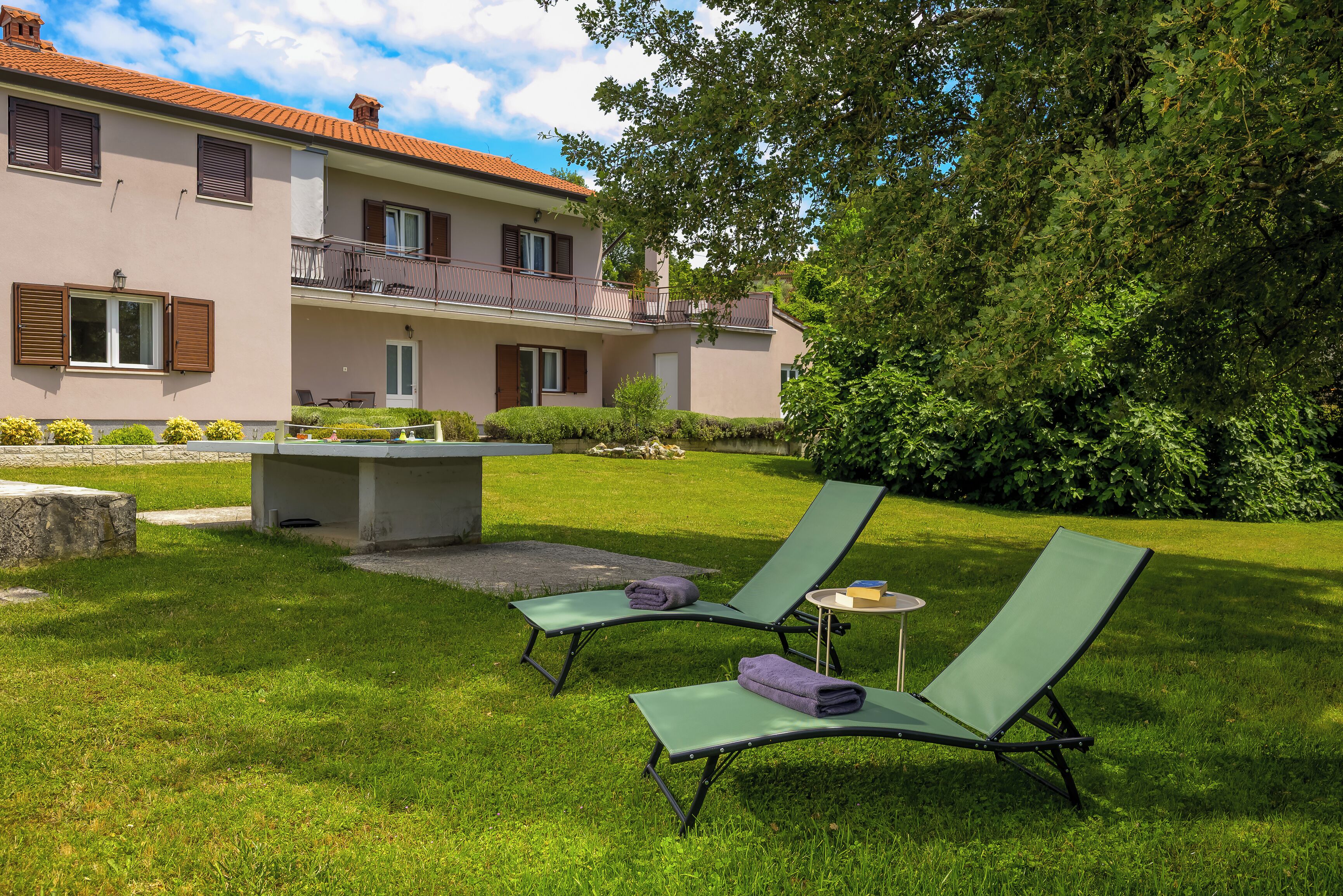 Ein zweistöckiges Gebäude mit Balkon, Rasen und zwei Liegestühlen mit Handtüchern.