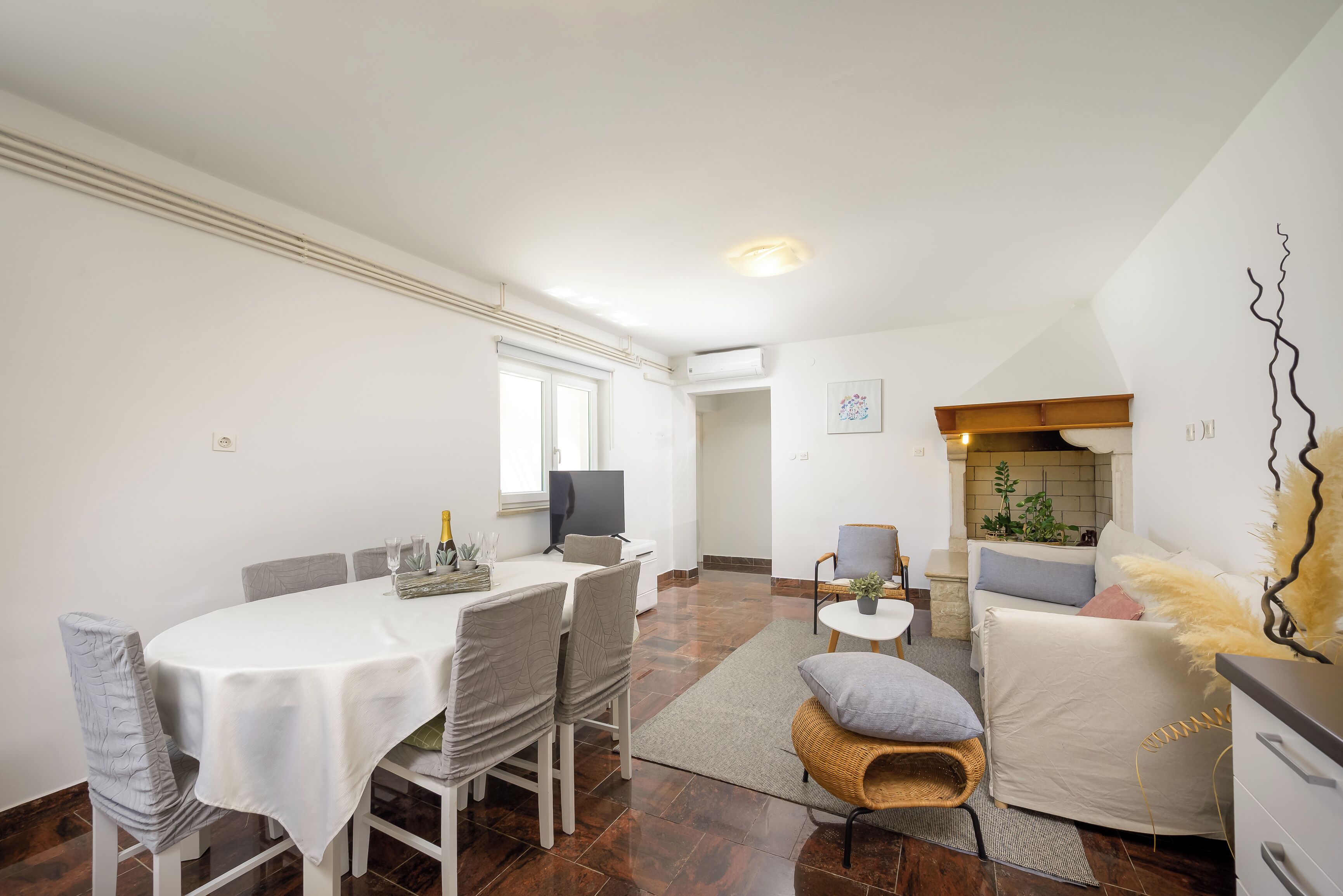A dining area with a table, chairs, and a television. There is a living area with a sofa and a small table.