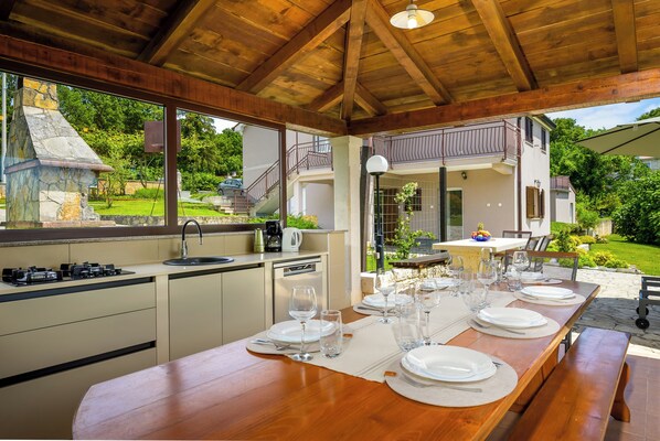 Una cocina moderna con comedor listo para una comida, que presenta un gran comedor de madera, un lavaplatos integrado y vistas al jardín.