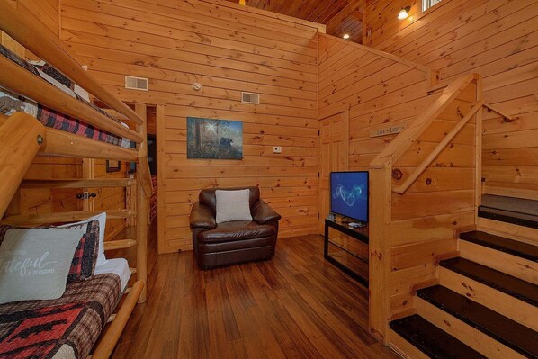 A cozy cabin interior with a wooden staircase, a leather sofa, a television, and a painting on the wall. - Moonlight Memories Cabin Rental (Pigeon Forge)
