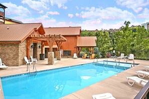 A swimming pool with lounge chairs and a wooden building with stone walls. - Moonlight Memories Cabin Rental (Pigeon Forge)