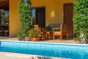 Ein Poolbereich mit einer Holzbank, einer Couch und einem Blumentopf mit roten Blüten.