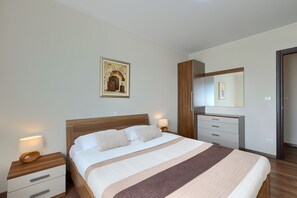 Ein Schlafzimmer mit einem Bett, Nachttischen, einer Kommode, einem Spiegel und einem gerahmten Bild an der Wand.