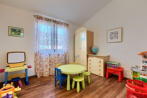 Ein Kinderzimmer mit Holzboden, einem runden Tisch und zwei Stühlen, einem Spielzeugfernseher und einem Globus auf einem Schrank.
