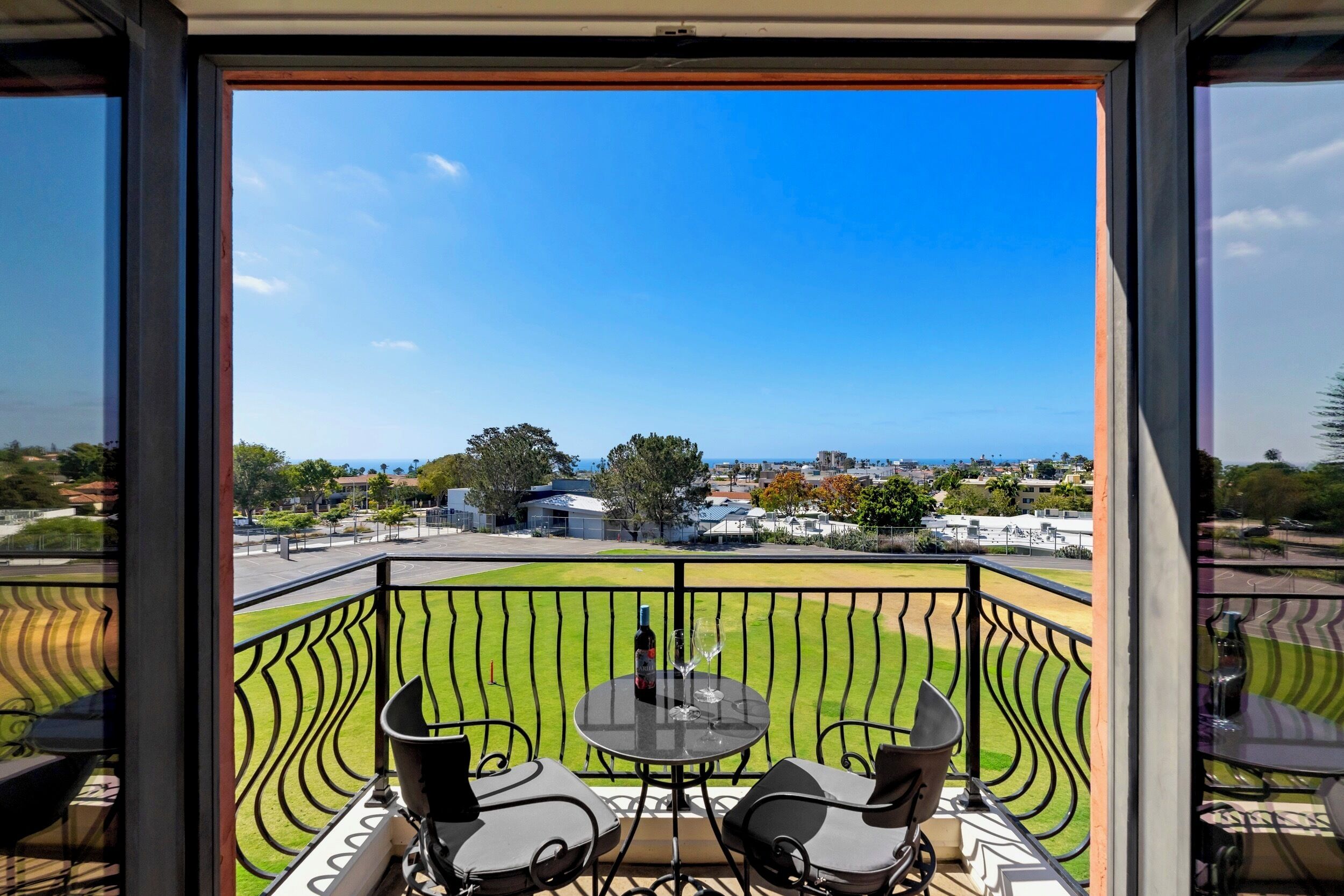 Ein Balkon mit Tisch und Stühlen, der auf ein Wohngebiet mit Häusern und einem klaren Himmel blickt.