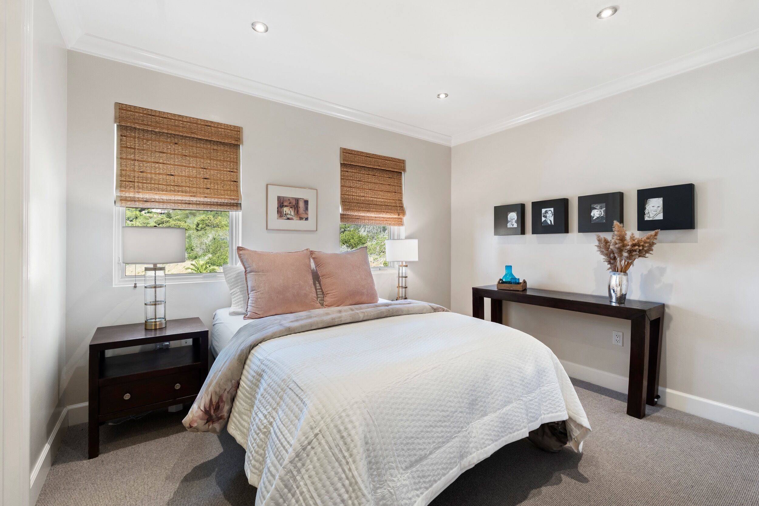 A bedroom with a bed, bedside tables, a nightstand, a console table, and a wall with framed pictures.