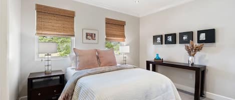 A bedroom with a bed, bedside tables, a nightstand, a console table, and a wall with framed pictures.