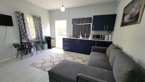 A living room with a sofa, a dining table with chairs, a kitchen area with cabinets and appliances, and a TV mounted on the wall. - New Listing-Bungalow Verde Unit Two (Castries)