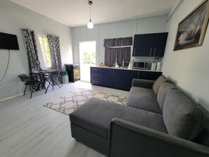 A living room with a sofa, a dining table with chairs, a kitchen area with cabinets and appliances, and a TV mounted on the wall. - New Listing-Bungalow Verde Unit Two (Castries)