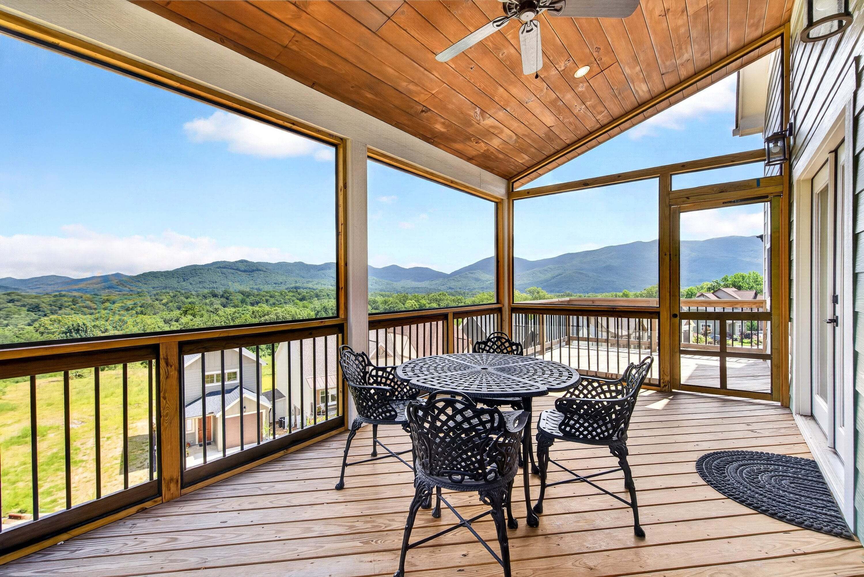 A covered outdoor area with a table and chairs, large windows, and a view of mountains.