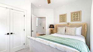 Un dormitorio con cama, armario, ventilador de techo y dos marcos con cuadros.