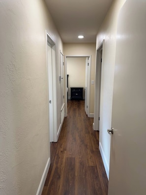 A hallway with wooden flooring and white walls, leading to a room with a dark-colored dresser.
