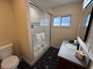 A bathroom with a glass shower enclosure, a toilet, a sink with a mirror, and a patterned floor. - Spacious 4-bedroom house in tranquil Clovis with AC (Clovis)