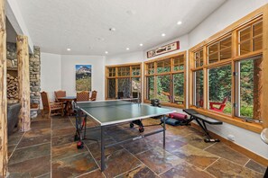 A ping pong table in a room with stone walls, large windows, and a stone fireplace. - Luxury Mountain Retreat with Panoramic Views, Hot Tub, Game Room, & Endless Outdoor Living (Durango)