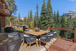 An outdoor deck with a wooden table and chairs, surrounded by a wooden railing, overlooking a forested mountain area. - Luxury Mountain Retreat with Panoramic Views, Hot Tub, Game Room, & Endless Outdoor Living (Durango)