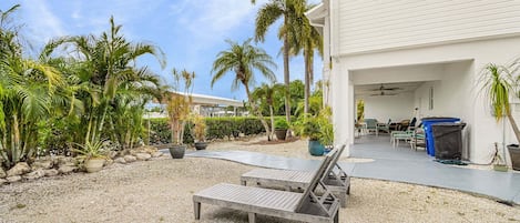 Een overdekt terras met loungezetels, een barbecue en plantenpotten.