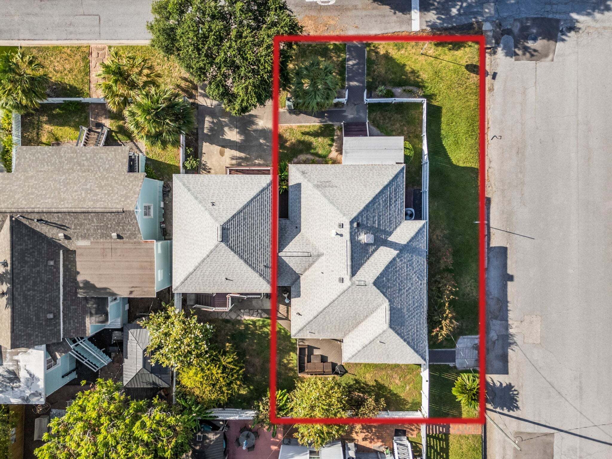 An aerial view of a residential area with multiple houses, a clear road, and a red boundary line.