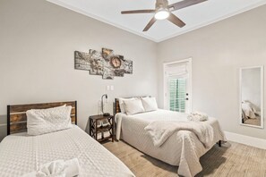 A bedroom with two beds, a ceiling fan, a wall-mounted artwork, and a door with a window. - Blue Palms- Steps away from OCEAN (Galveston)