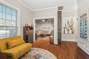 A living room with a yellow sofa, a fireplace, and a dining area with a table and chairs. - Blue Palms- Steps away from OCEAN (Galveston)