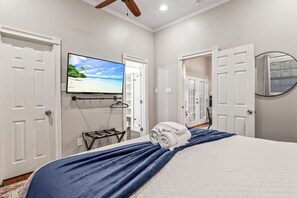 A bedroom with a bed, a TV mounted on the wall, and a door leading to another room. - Blue Palms- Steps away from OCEAN (Galveston)