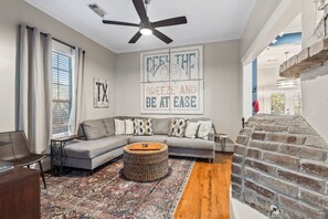 A living room with a sectional sofa, a coffee table, a patterned rug, a fireplace, and a ceiling fan. - Blue Palms- Steps away from OCEAN (Galveston)