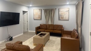A living room with a flat-screen TV, a brown leather sofa, a coffee table, and two armchairs. - Spacious 5-Bedroom Home Near Atlanta Airport Area (Atlanta)