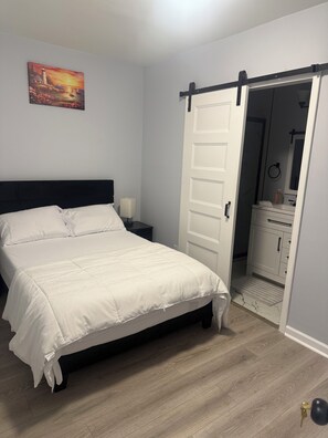 A bedroom with a bed, a nightstand, a painting, and a sliding door leading to a bathroom. - Spacious 5-Bedroom Home Near Atlanta Airport Area (Atlanta)