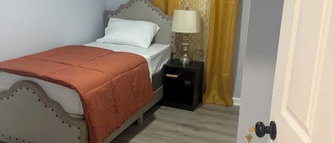 A bedroom with a bed, a nightstand, a lamp, a ceiling fan, and a door.