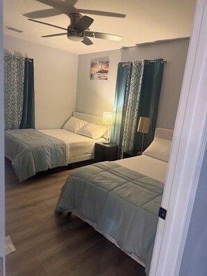 Ein Hotelzimmer mit zwei Betten, einem Deckenventilator, einem Nachttisch mit Lampe und einem Gemälde an der Wand.