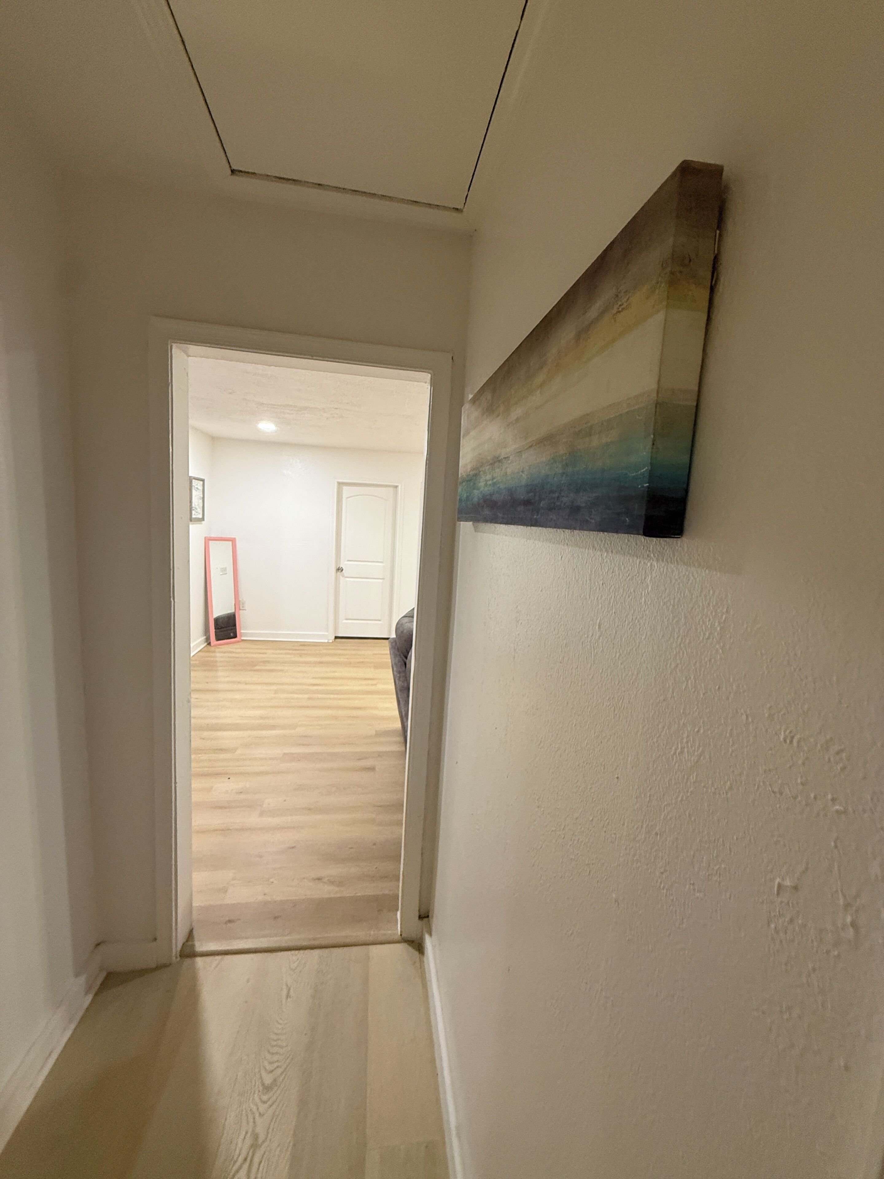 A hallway with a wooden floor leading to a room with a door.
