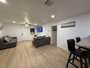 Ein modernes Wohnzimmer mit einer Couch, einem Esstisch mit Stühlen, einem flachbildfernseher an der Wand und einem Deckenventilator.
