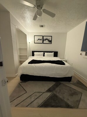 Ein Schlafzimmer mit einem Bett, einem Deckenventilator, einer Wand-Klimaanlage und zwei gerahmten Bildern.