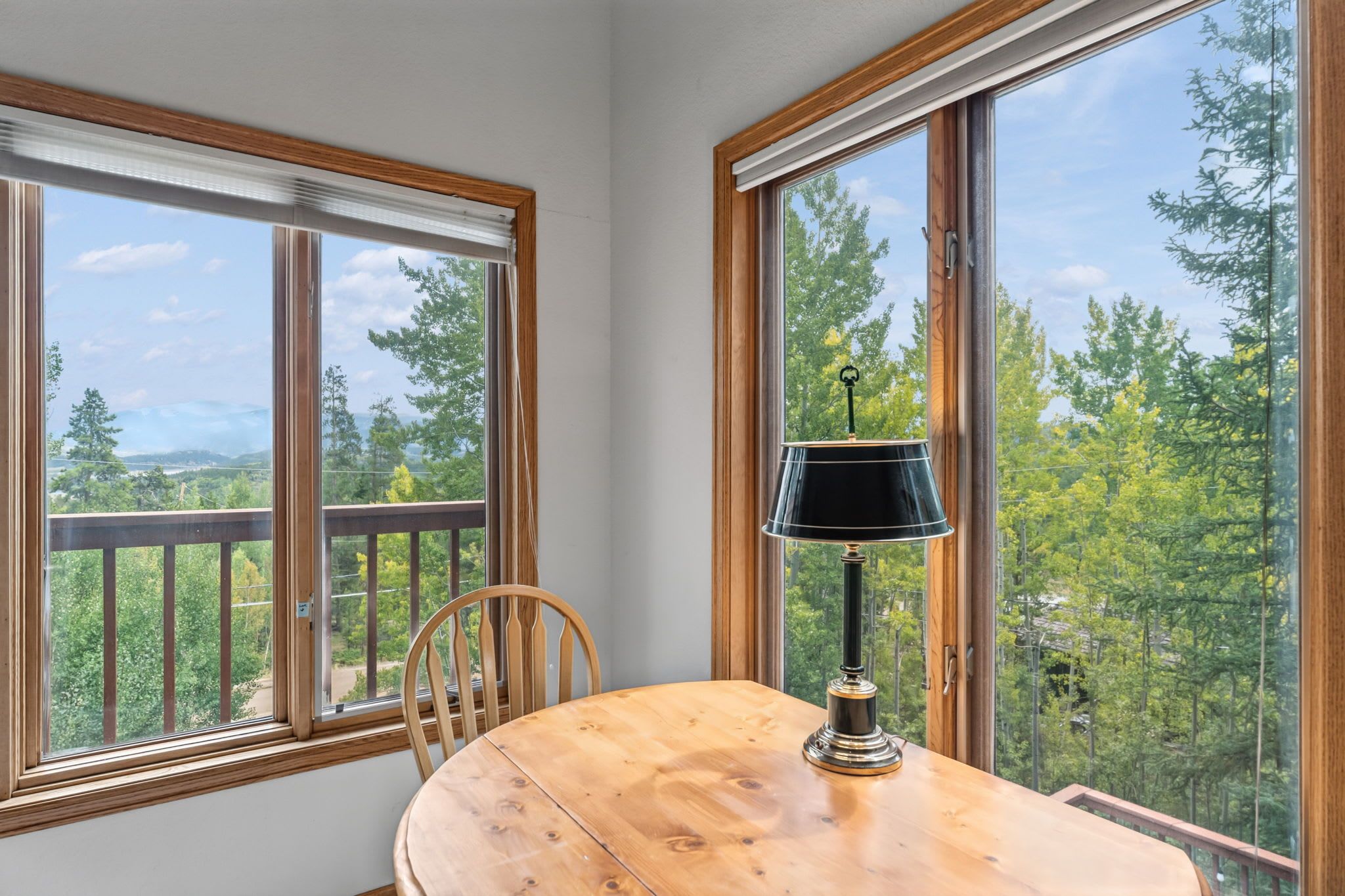 A room with a wooden table and chairs, large windows with a view of trees and mountains, and a lamp on the table.