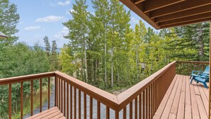 A wooden deck with a railing overlooking a forested area.