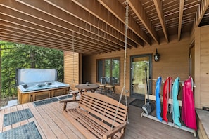 A wooden deck with a hot tub, outdoor seating, and a covered area with a grill.