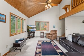 A spacious living area with a ceiling fan, a television, a leather sofa, a coffee table, and a rug. - Red Bird Retreat | Arctic Hot Tub | Stunning Views (Silverthorne)